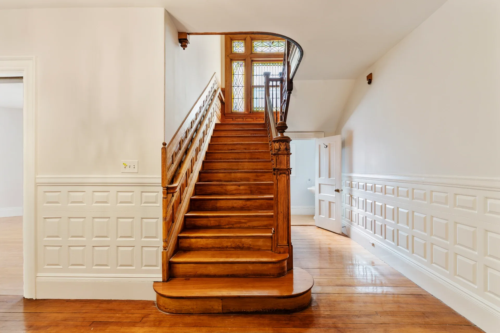 Existing entry hall at 62 Fuller Street with a carved wood staircase, paneled walls, and stained-glass landing window before renovation