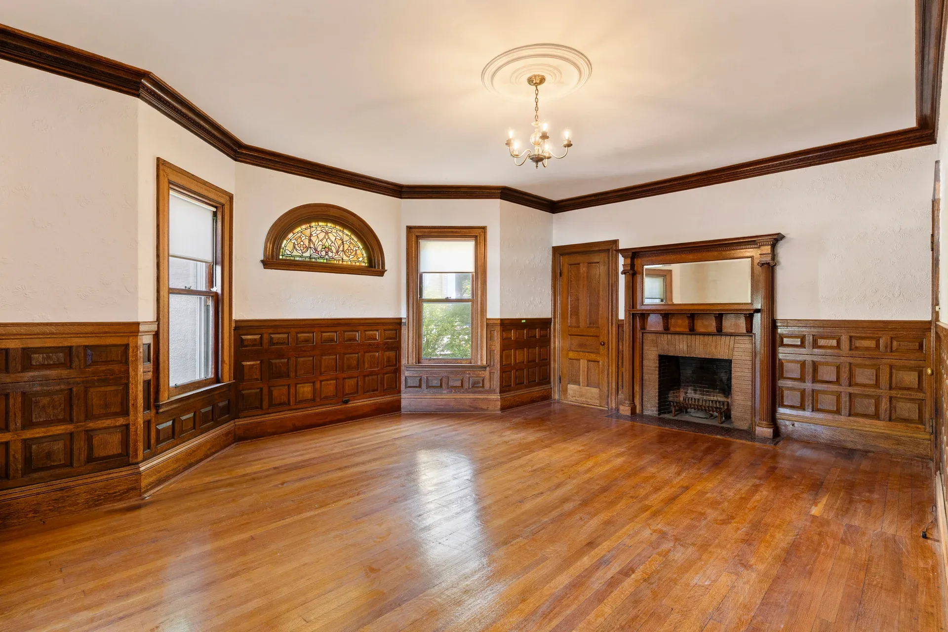 Existing parlor at 62 Fuller Street with dark wood paneling, a fireplace, and an arched stained-glass window before renovation